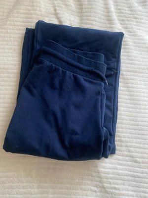 Mörkblå mjukisbyxor med resårmidja - Säljer ett par mörkblå mjukisbyxor i mjukt och skönt material. Byxorna har resår i midjan och raka ben, perfekta för chill dagar hemma eller när du vill vara bekväm. Klassisk modell utan synliga loggor eller detaljer.