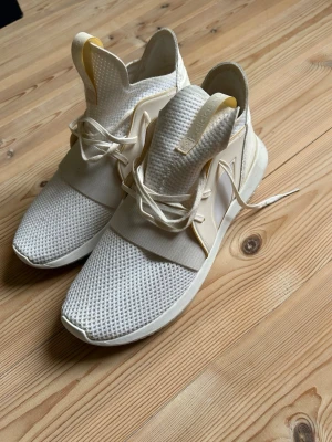 Adidas Tubular Defiant White - Snygga vita sneakers från Adidas med mesh-ovandel och elastiskt band över foten. Skorna har vita snören och en chunky sula. Perfekta för dig som gillar sportig och modern stil. Nypris 1399kr, använda enstaka gånger. 
