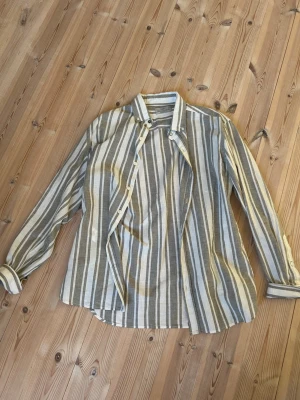 Randig skjorta från Mango - Säljer en snygg randig skjorta från Mango i beige och grå toner. Regular fit-modell med knappar framtill. Perfekt för en avslappnad och stilren look. Storlek S men passar även M. 