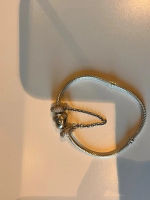 SilverfärgadEn säkerhets kedja från Pandora  ÄKTA - En säkerhets kedja från Pandora, silvrig kedja med stenar/diamanter på ringarna. Kedjan använder man som både prydnad och säkerhet för att berlockerna inte åker av från armbandet.