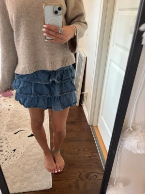 Blå jeans volangkjol - Supersöt jeanskjol med flera volanglager. Kjolen har en mörkblå dragkedja i sidan.