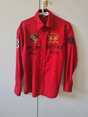 Barn skjorta med Porsche Polo Team tema - Röda långärmade bomull skjorta från samarbete mellan La Martina och Porsche Polo Team Skjorta har broderade logotyper. Storlek 146/152.