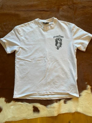 Vit t-shirt med tryck - Vit t-shirt med svart tryck på bröstet som föreställer en joker med spelkort och texten 'Grave Fame'. Klassisk passform och rund hals. 