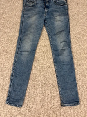 Blå slim fit jeans med slitningar - Snygga blå slim fit jeans med lätt slitna detaljer och klassisk femficksdesign. Jeansen har normal midja och raka ben med diskreta tvättade partier framtill och bakfickor med dekorativa sömmar. Perfekta för en avslappnad och trendig look.