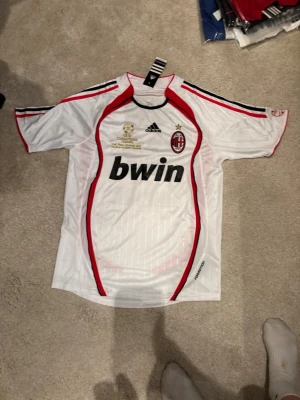 AC Milan retro tröja #22 kaka - Vit AC Milan matchtröja från Adidas med röda och svarta detaljer, Champions League-final 2007-tryck, klubbmärke och sponsorlogga framtill. KAKA och nummer 22 på ryggen. Perfekt för fotbollsfans som vill sticka ut på planen eller läktaren.