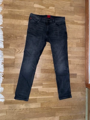 Svarta slim fit jeans från HUGO - Snygga svarta slim fit jeans från HUGO med klassisk femficksdesign. Jeansen har en röd patch med logga bak i midjan och är tillverkade i stretchigt denim för extra komfort. Perfekta för en trendig och avslappnad look.//PRIS KAN DISKUTERAS!!