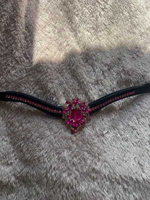 Svart pannband med rosa strass - Jätte fint pannband med rosa pärlor. Storlek cob. Säljer pga att de är förstora för min häst med litet huvud. Den stora ”kristallen” är fast stripad och märke finns ej pga jag köpte av en egenföretagare.