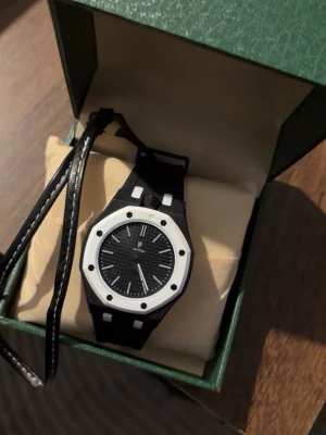 Klocka - Snygg svart klocka med vit ram och svart urtavla med vita detaljer. Klockan har en modern, sportig design och ett svart band i syntetmaterial. Perfekt accessoar för dig som gillar stilrena och kontrasterande färger.