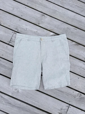 Ljusgråa klassiska shorts - Snygga ljusgrå shorts med klassisk passform och diskreta fickor fram och bak. Stängs med knapp och dragkedja. Perfekta för en stilren och enkel look. Materialet ser ut att vara bomull eller linneblandning för en luftig känsla.