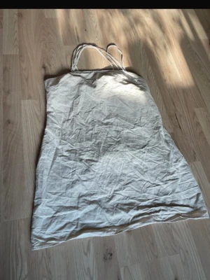 Beige linneklänning med smala axelband - Säljer en enkel och stilren beige klänning i linne med smala axelband. Klänningen har rak passform och är lätt och luftig, perfekt för varma dagar. Materialet ger en naturlig och avslappnad look.