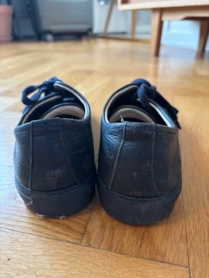 Marinblå axel arigato skor - Mörkblå ARIGATO sneakers i läder, storlek 40. Välanvända med tydliga bruksspår som syns på bilderna, men fortfarande snygga och har mycket användning kvar. Stilrena och passar till det mesta!