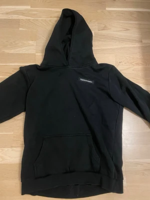 Svart hoodie från Peak Performance - Säljer en svart hoodie från Peak Performance med klassisk logga på bröstet. Hoodien har stor huva och en rymlig magficka. Tillverkad i mjukt bomullsmaterial och har ribbade muddar vid ärmslut och nederkant. Perfekt för en avslappnad och stilren look.