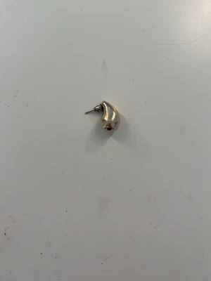 Guldfärgat droppformat örhänge - Säljer ett stilrent örhänge i guldfärgad metall med droppformad design. Perfekt till er som har tappat bort det andra örhänget.