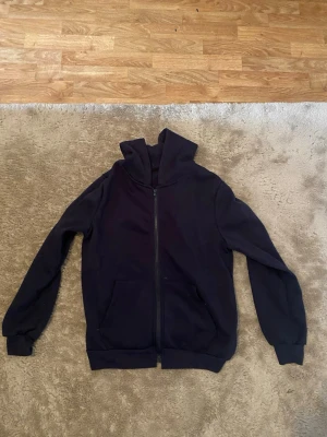 Mörkblå zip hoodie med hög krage - En enkel och stilren mörkblå hoodie med dragkedja framtill och två fickor. Hoodien har en hög krage och ribbade muddar vid ärmslut och nederkant. Perfekt för dig som gillar en clean look och vill ha något bekvämt att slänga på sig.