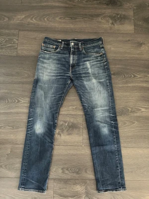 Levis Jeans 502 - Säljer ett par mörkblå Levis jeans med raka ben och snygga slitningar på framsidan. Klassisk femficksmodell med knappgylf och kontrastsömmar. Jeansen har en cool tvättad look och passar perfekt till en avslappnad stil. Hör gärna av dig vid funderingar 😊