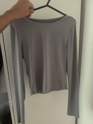 Grå långärmad topp - En enkel och stilren grå långärmad topp med rund halsringning. Perfekt att matcha med jeans eller kjol för en clean look. Materialet känns mjukt och stretchigt, vilket gör den bekväm att bära hela dagen.