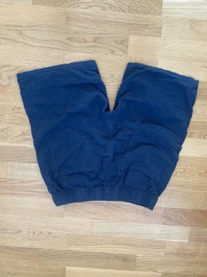 Mörkblå linneshorts med snörning - Snygga mörkblå shorts med elastisk midja och vit snörning framtill. Shortsen har två sidofickor och två bakfickor, perfekta för en avslappnad stil. Tillverkade i ett mjukt material som känns skönt mot huden.