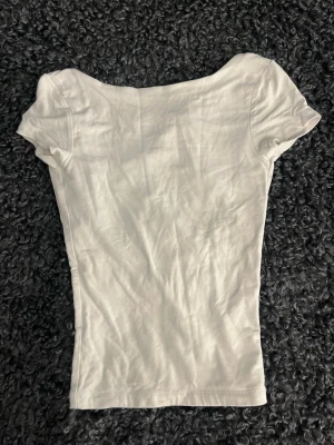 Vit topp med öppen rygg - Snygg vit topp i mjukt material med korta ärmar och en djup, öppen rygg. Perfekt för dig som vill ha en enkel men ändå unik topp till din outfit. Passformen är tight och toppen är enkel att matcha med olika stilar.
