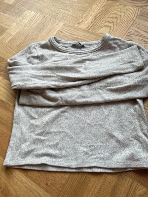 Beige långärmad tröja från Zara - Mjuk och enkel beige långärmad tröja från Zara TRF. Tröjan har rund halsringning och är tillverkad i ett tunt, bekvämt material som passar perfekt till lager på lager. Stilren och lätt att matcha med olika outfits.