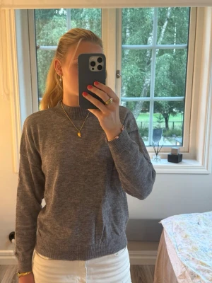 Grå stickad tröja med ribbad krage -  grå stickad tröja med hög ribbad krage och långa ärmar. Materialet är mjukt och bekvämt, perfekt för kyligare dagar.