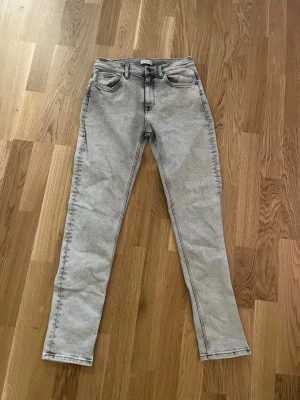 Ljusgrå raka jeans - Säljer ett par ljusgrå jeans med rak passform och klassisk femficksdesign. Jeansen har normal midja och svarta kontrastsömmar. Tillverkade i ett mjukt denimtyg som passar perfekt till en avslappnad stil.