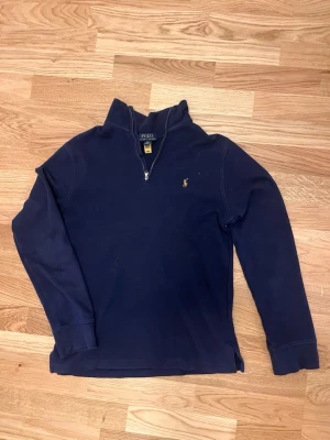 Mörkblå halvzip från Polo Ralph Lauren - Snygg mörkblå tröja från Polo Ralph Lauren med halvzip och klassisk flerfärgad broderad logga på bröstet. Tröjan har hög krage och långa ärmar, perfekt för lager på lager. Tillverkad i mjukt bomullsmaterial.