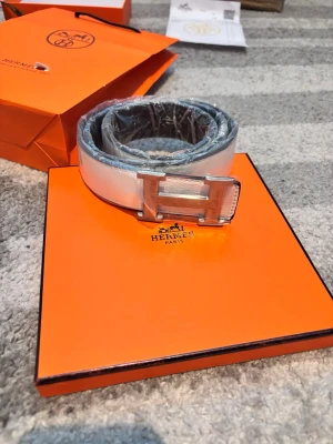 Vitt  bälte med silverdetaljer - Snyggt vitt bälte med klassiskt H-spänne i silverfärg. Bältet har en stilren och modern look som passar till många outfits. Levereras med originalförpackning och påse.