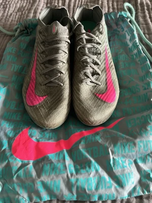 Nike fotbollsskor grå med rosa swoosh - Säljer ett par blåa Nike fotbollsskor med stora rosa swoosh-loggor på sidorna. Dem är i hyfsat skick då dem använts en del fast men har fortfarande mycket mer i sig. Priset är inte hugget i sten och kan även reduceras ifall du vill köpa flera av mina skor. Skriv gärna och fråga om du har några funderingar!