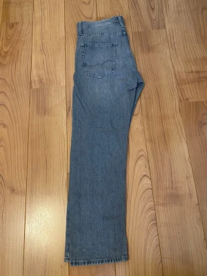Grå raka jeans med hög midja - Ett par klassiska blå jeans med rak passform och hög midja. Jeansen har en bakficka och en enkel design utan slitningar eller dekorationer. Perfekta för en avslappnad och stilren look. Materialet ser ut att vara bomullsdenim.