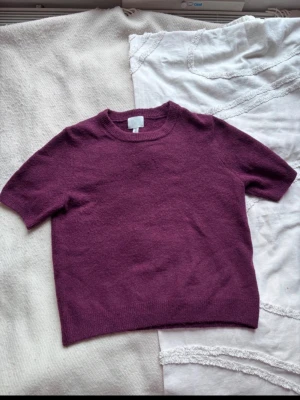 Vinröd  stickad t-shirt från H&M - Kortärmad stickad t-shirt i vinröd från H&M. Tröjan har rund halsringning och ribbade kanter. I fint skick. Säljer då tröjan inte används.