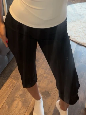 Svarta midwaist shorts - Säljer ett par svarta midwaist capris i knälång modell. De har en enkel och clean design utan synliga detaljer och är perfekta för en avslappnad look. Materialet känns mjukt och stretchigt, vilket gör dem riktigt bekväma att bära.