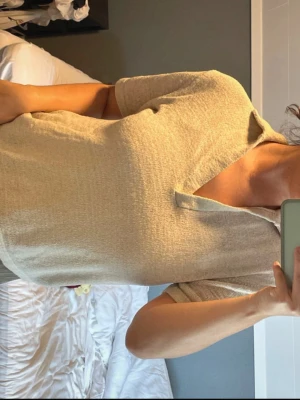 Beige kortärmad topp med krage - Säljer en beige topp med korta ärmar och krage. Toppen har en v-ringad öppning framtill och är gjord i ett mjukt, strukturerat material som känns skönt mot huden. Passformen är normal och toppen är enkel att styla till olika looks.