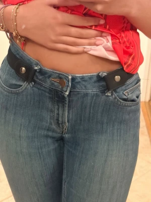 Svart elastiskt knappbälte - Säljer ett svart elastiskt bälte som fästs med knappar istället för traditionellt spänne. Perfekt för jeans och ger en clean look utan synligt spänne framtill. Bältet är justerbart och sitter bekvämt runt midjan.