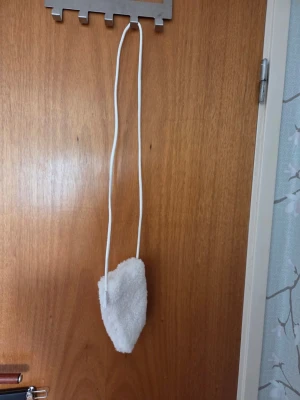 Vit fluffig mobilväska  - Supersöt vit mobilväska med fluffigt, mjukt material. Väskan har en lång vit rem och stängs med tryckknapp. Perfekt för dig som gillar gulliga accessoarer och vill sticka ut lite extra.