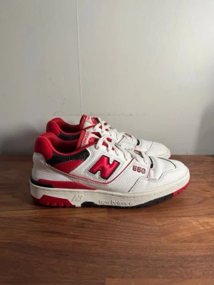 New Balance 550 vita/röda sneakers - Snygga New Balance 550 sneakers i vitt läder med röda och svarta detaljer. Klassisk låg modell med tydlig logga på sidan och röd sula. Perfekta för dig som gillar retrostil och streetwear. Skön passform och tidlös design.