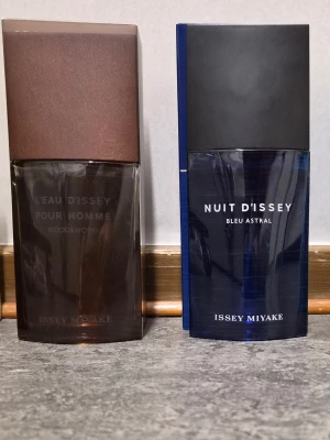 Sälj eller byte Issey Miyake herrparfymer duo - Två stilrena herrparfymer från Issey Miyake: L'Eau d'Issey Pour Homme Wood&Wood i brun glasflaska med trälock och Nuit d'Issey Bleu Astral i djupblå glasflaska. Båda flaskorna har en modern, kantig design och tydliga logotyper på framsidan.