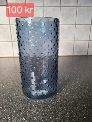 Blå vasmed bubblig struktur - Säljer eb hög blått vas med bubblig struktur på utsidan. Glaset är cylinderformat och har en modern look med prickigt mönster i glaset. Perfekt för drycker eller som dekoration i köket.