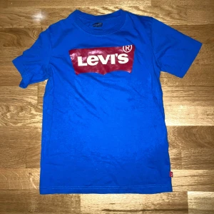 T-shirt från Levi’s - Säljer en ny blå t-shirt från Levi’s med röd logga på bröstet med texten ”LEVI’S” i vitt. T-shirten e helt ny men saknar prislapp.