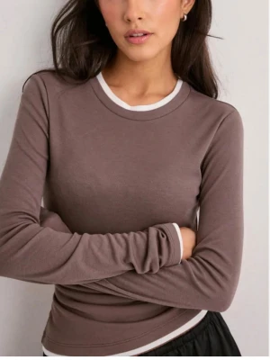 Taupe långärmad topp från Nelly - Säljer en brun långärmad topp från Nelly i mjuk bomull. Toppen har en vit kontrastkant vid halsringningen och nederkanten, vilket ger en sportig och clean look. Perfekt att styla med jeans eller kjol för en enkel men snygg outfit.