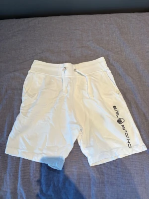 Vita shorts från Sail Racing - Snygga vita shorts från Sail Racing med snörning i midjan och tryckt logga längs benet. Shortsen har två sidofickor och är perfekta för sommardagar. Tillverkade i mjukt material för skön passform.
