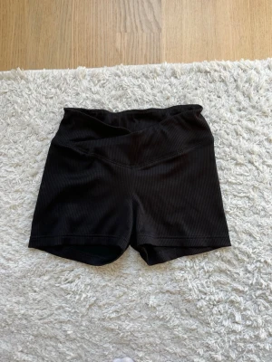 Svarta ribbade träningsshorts - Säljer ett par svarta ribbade shorts med medel midja. De har en tight passform och är perfekta för både chill och träning. Materialet känns mjukt och stretchigt, vilket gör dem riktigt bekväma att bära.