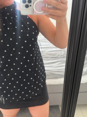 Svart prickig kort klänning - Säljer en svart kort klänning med vita prickar och hög hals. Klänningen är ärmlös och har en slim passform som sitter snyggt på kroppen. Perfekt för dig som gillar en enkel men trendig look. Kyt baktill. Nypris 299