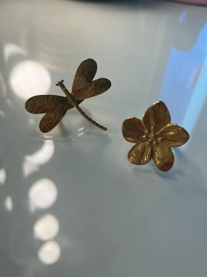 två guldfärgade ringar  - Två Guldiga ringar. En blomma med fina detaljer på bladen och en trollslända. Använda fåtal gånger💕