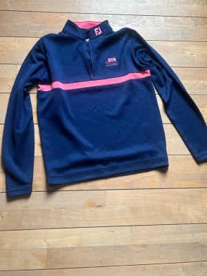 Mörkblå sporttröja med rosa detaljer - Snygg mörkblå sporttröja från FootJoy, Perfekt för golf eller annan träning. Materialet känns mjukt och stretchigt. Den är helt ny och oanvänd!