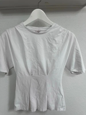 Vit t-shirt från Nelly - Säljer en vit t-shirt från Nelly i storlek XXS. T-shirten har korta ärmar, rund halsringning och en figurnära passform. Tillverkad i mjuk bomull, perfekt för en clean och enkel look.