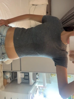 Mörkgrå croppad t-shirt - Säljer en enkel och stilren mörkgrå croppad t-shirt med rund hals och korta ärmar. Perfekt till jeans eller kjol för en avslappnad look. Materialet känns mjukt och stretchigt, vilket gör den bekväm att bära hela dagen.