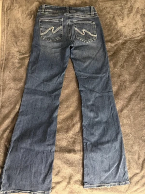 Blå bootcut jeans med broderade fickor nelly  - Säljer ett par blå bootcut jeans med snygga broderade detaljer på bakfickorna. Endast använda 1 gång och köpte dem för 700kr. Storlek 38 men passar även 36.   Jeansen har klassisk femficksmodell, låg midja och är tillverkade i mjukt denimtyg. Perfekta för dig som gillar en avslappnad men trendig look.