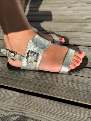 Silvriga lädersandaler från Blankens - Snygga sandaler i silverfärgat läder från Blankens. Modellen har två breda remmar med justerbara metallspännen och en svart sula. Perfekta för sommaren och ger en cool touch till din outfit.