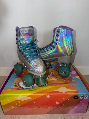 Holografiska rullskridskor Impala - Säljer ett par riktigt snygga holografiska rullskridskor från Impala. Dem är använda 2 gånger bara. De har högt skaft, blå glittrande snören och turkosa hjul. Perfekta för dig som vill sticka ut på rinken eller gatan. Kommer i originalkartong med färgglad design. 