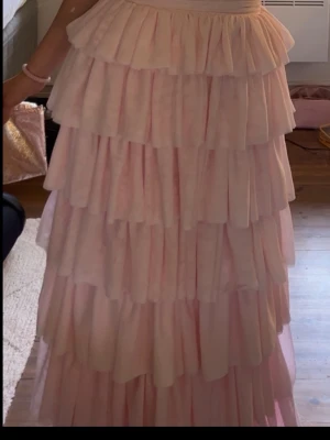 Ljusrosa långklänning med volanger - Supersöt ljusrosa långklänning med flera lager volanger och djup v-ringning i ryggen.💃 Klänningen är ärmlös och har en romantisk look som passar perfekt till olika tillfällen t.ex. på bal som jag använde klänningen till, därav är den endast använd vid ett tillfälle. 